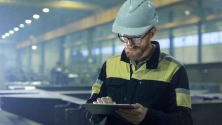 Engineer in hardhat is using a tablet computer in a heavy industry factory.
